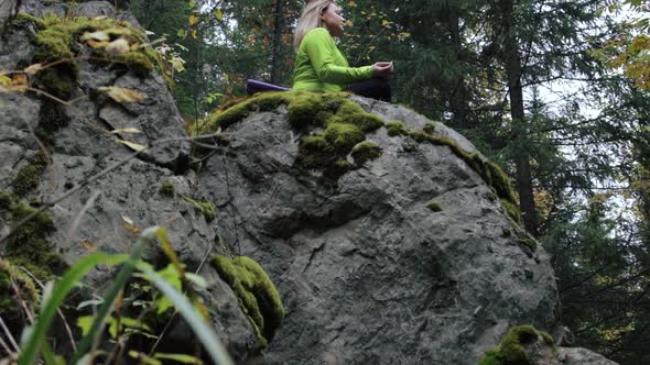 Woman meditating on a rock in the forest