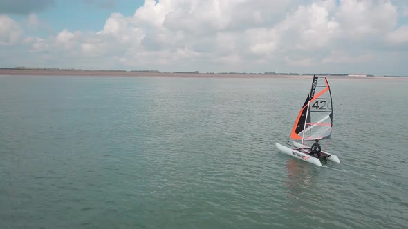 Man sailing his catamaran in the sea. Drone pans to the side, beautiful coastal landscape.