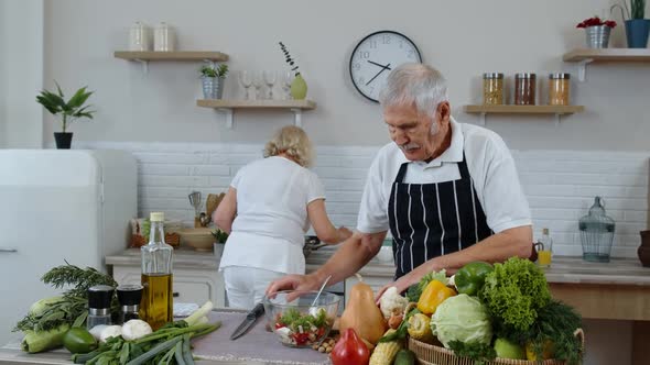 Elderly Grandparents in Kitchen Interior. Senior Woman and Man Cooking Salad with Fresh Vegetables