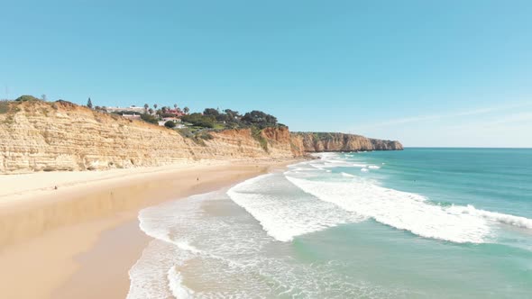 Waves washing on sand beach and cliffs of Lagos coastline. Aerial forward