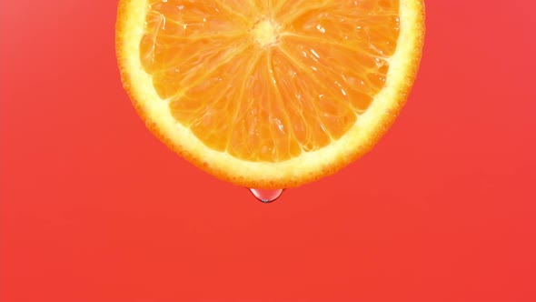 Water drop falling from orange hue orange on red background. Orange slice and water splashing