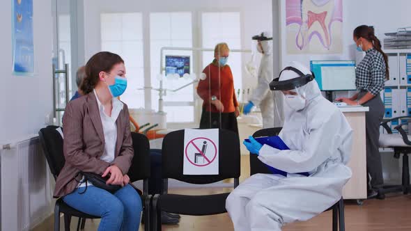 Dentist Nurse with Protection Equipment Talking with Patient