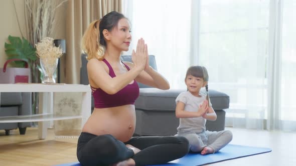 Asian young pregnant woman doing yoga pilates workout in living room.