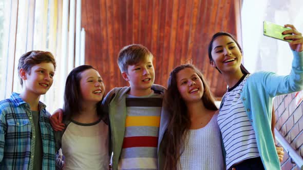 Smiling schoolkids taking selfie with mobile phone in corridor