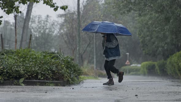 Slow motion of a young boy jumping in the pouring rain holding an umbrella