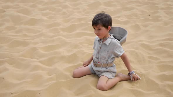 Boy Child is Sitting on a Dune in the Clothes of a Traveler