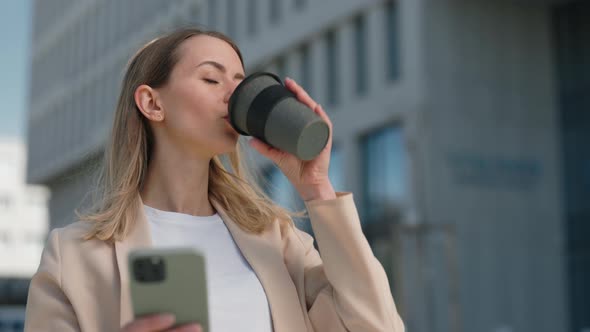 Woman Using Smartphone and Enjoying Hot Beverage on Street