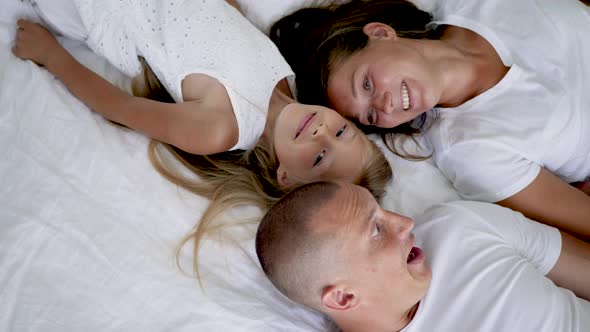 Family with Two Children Lie on a White Big Bed