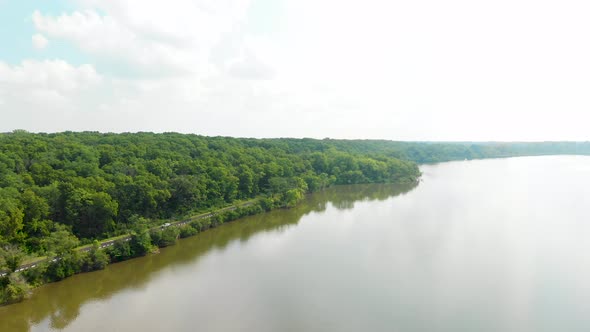 drone forward flight into the horizon over a lake in a forest with lush green trees and sunny blue s