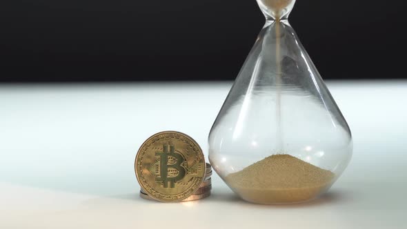 Gold Bitcoin and Hourglass on White Table with Black Background. Macro Shot. Time Is Money. Sand