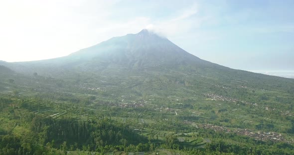 Slow aerial forward flight over rural plantation with Merapi Volcano in background
