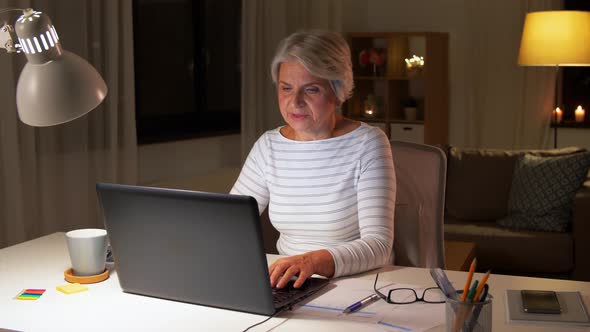 Happy Senior Woman with Laptop at Home in Evening