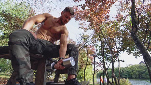 Shirtless sportsman lifting dumbbell outdoors