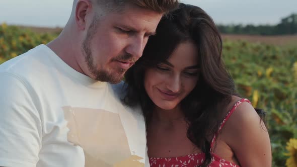 Happy Couple Looking on Picture Together and Smiling Among Sunflowers