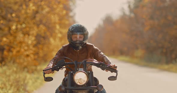 Young Guy in a Helmet Rides a Brutal Motorcycle on an Autumn Road