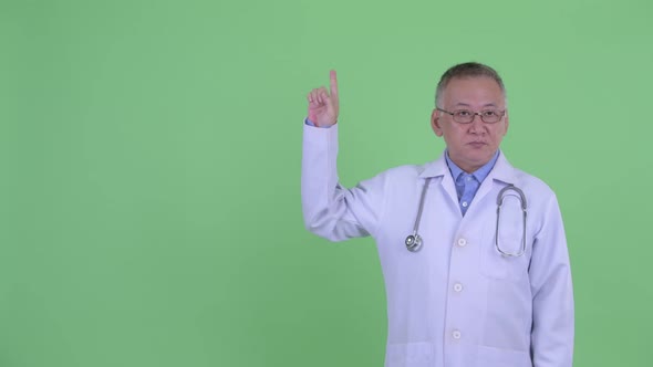 Happy Mature Japanese Man Doctor Talking While Pointing Up