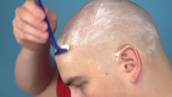 The Bald Young Man Insolently Shaves His Head Closeup. A Man Cuts His Hair with a Razor