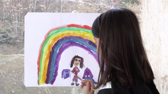 The girl is drawing a rainbow on the glass.