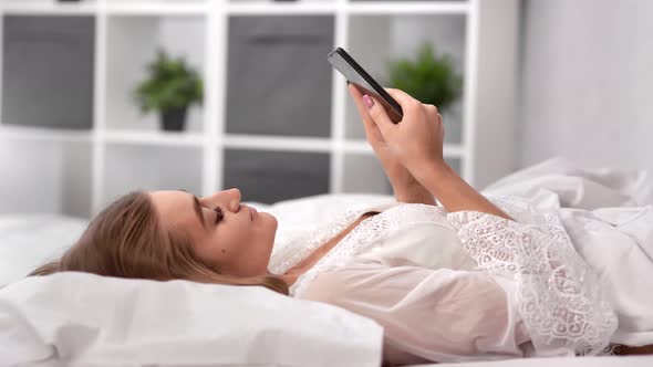 Relaxed Woman Lying on Comfy Bed Chatting Using Smartphone