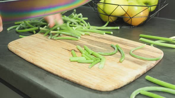 Woman cuts green beans on cutting board.