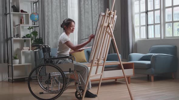 Asian Artist Girl In Wheelchair Holding Paintbrush Mixed Colour And Painting On The Canvas