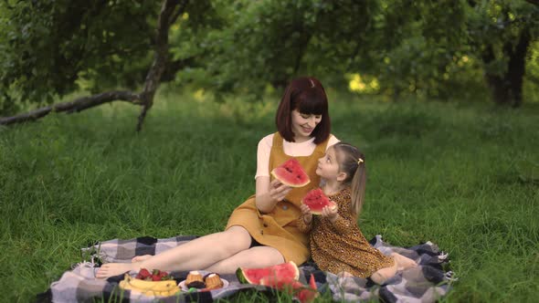 Young Mom with Her Little Cute Daughter on a Picnic in Green Park Eating Watermelon