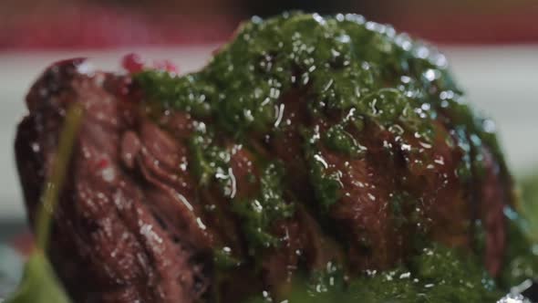 Close-up of juicy fried beef steak filet mignon on a plate with green herb sauce