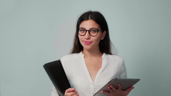 A Young Girl in Glasses with a Folder and a Tablet in Her Hands Looks at the Camera with a Smile