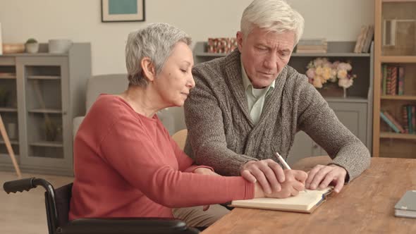 Man Helping Wife with Disability Writing