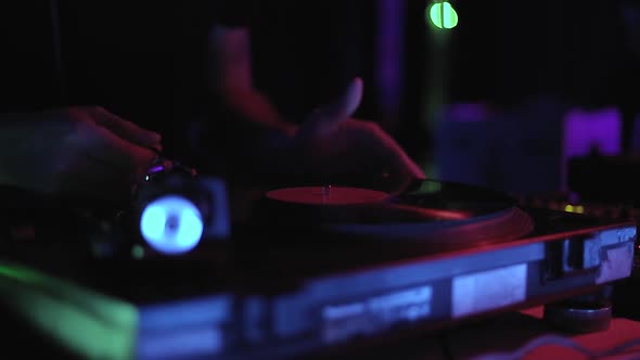 Video clip of dj playing vinyl record on turntables in night club in neon lights