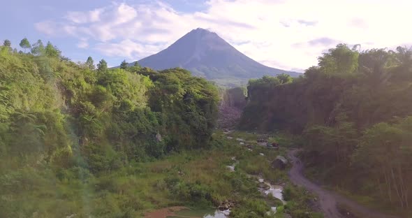 Ascending drone shot of over natural lake in nature with Merapi Volcano and Lava Path and Road durin