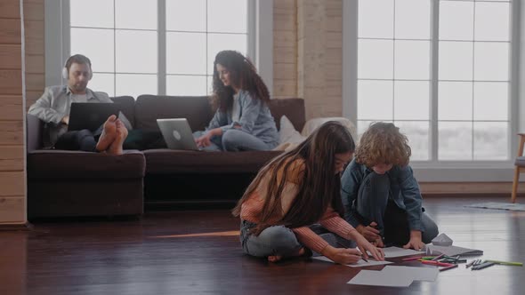 Children Draw on the Floor While Their Parents Sit on the Couch Working