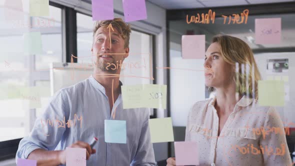 Professional businesswoman and businessman discussing over memo notes on glassboard in modern office