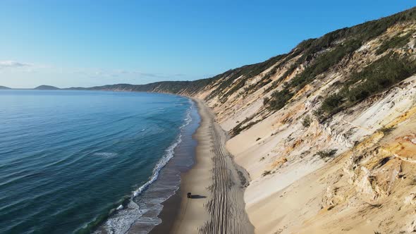 4wd car travelling between the ocean waves and a steep sand cliff on deserted coastline beach road.