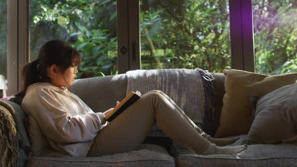 Asian girl smiling while reading a book while siting on the couch at home