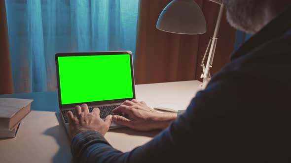 Over the Shoulder Shot of Bearded Unrecognazable Man Typing on Laptop with Green Screen at White