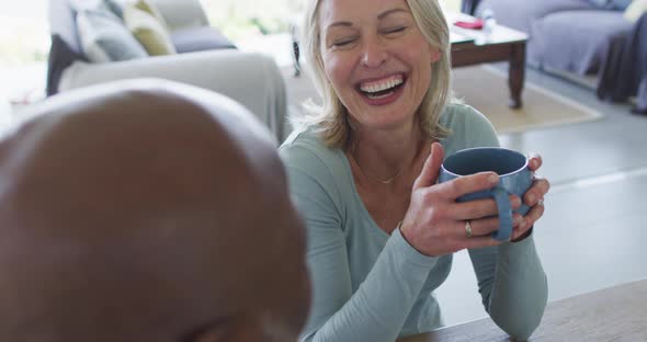 Caucasian senior woman holding a coffee cup smiling while talking to her husband at home