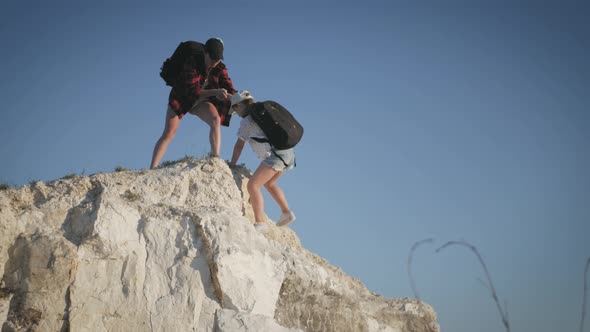 Girl Helps Her Friend Climb Up the Last Section of Mountain, Tourists with Backpacks Help Each Other