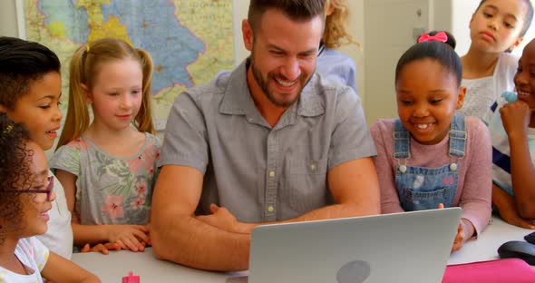 Caucasian male teacher teaching school kids on laptop in classroom at school 4k