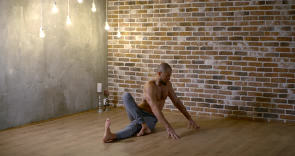 Adult Male Gymnast Is Lying in Pose for Stretching Legs and Hands Muscles in Training Hall