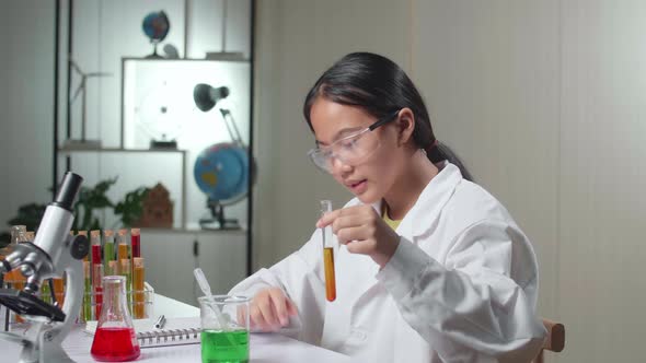 Young Asian Scientist Girl Mixes Chemicals In Test Tube And Note On Her Book