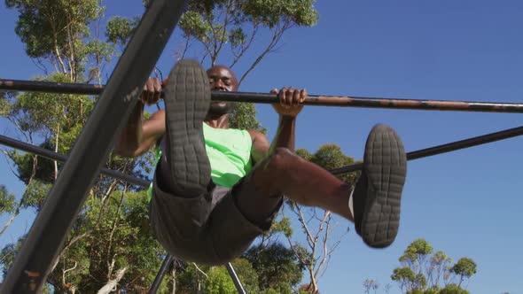 Fit african american man exercising outside, doing hanging pull ups on a climbing frame