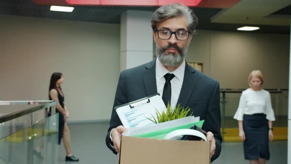 Sad Office Worker Walking in Hallway with Carton Box Leaving Work After Employment Termination