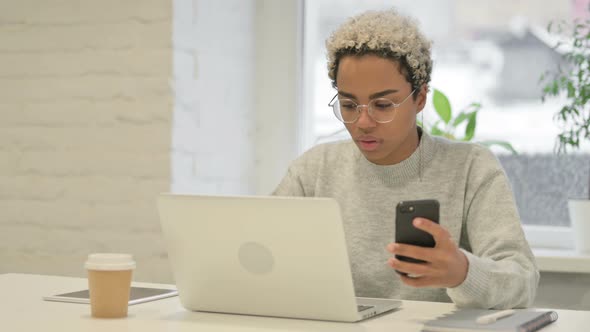 African Woman Using Smartphone While Using Laptop in Office