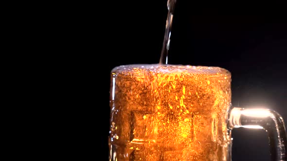 Low Angle of Soft White Foam Rising and Spilling From Glass Cup of Cold Beer on Black Background