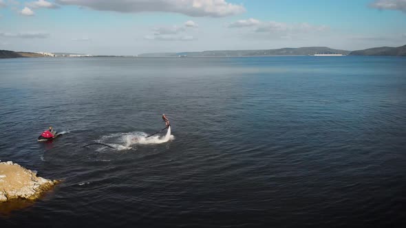 Sportsman Is Flying on Flyboard on Lake in Daytime, Performing Trick, Aerial Moving Around View