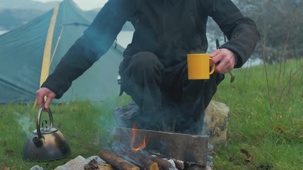 Man makes cup of hot coffee out camping by fireside