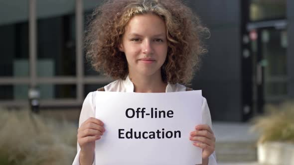 Cute Teenage Girl Stands with a Poster OFFLINE EDUCATION Near the School Building