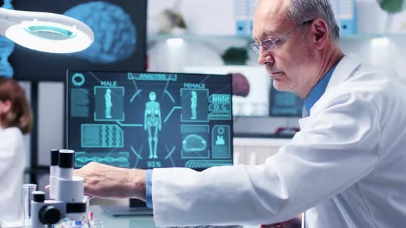 Medium Dolly Shot of Mature Chemist in His 60s Looking at Tubes with Samples alt