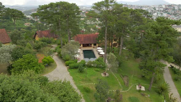 Aerial drone flying around the swimming pool between the pine trees with nice city landscape at back